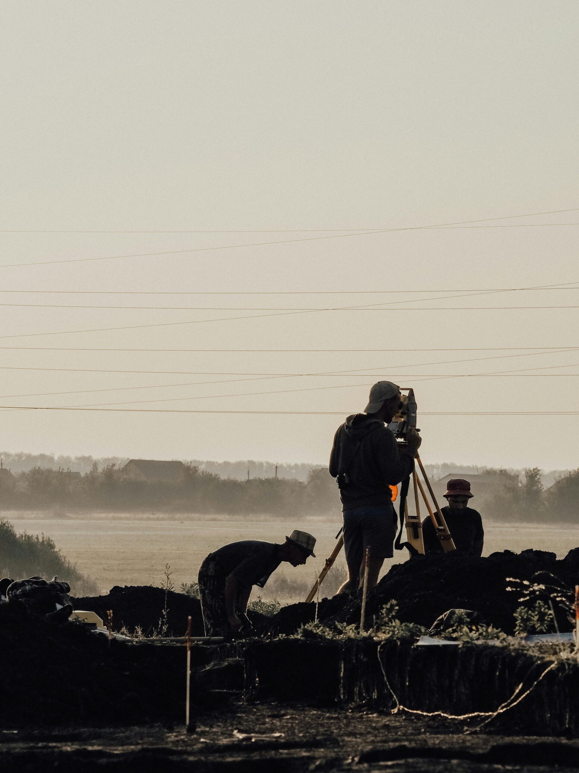 Group of surveyors using a theodolite at a construction site during a foggy morning with silhouettes visible.